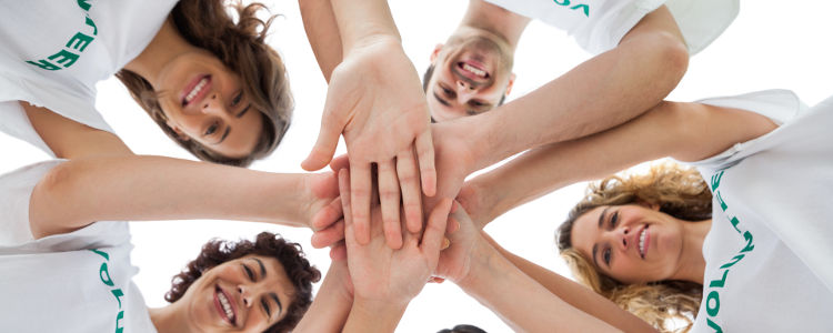 Cheerful group of volunteers putting hands together on white background